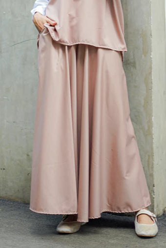 Person wearing a long pink skirt by Abame standing against a wall.