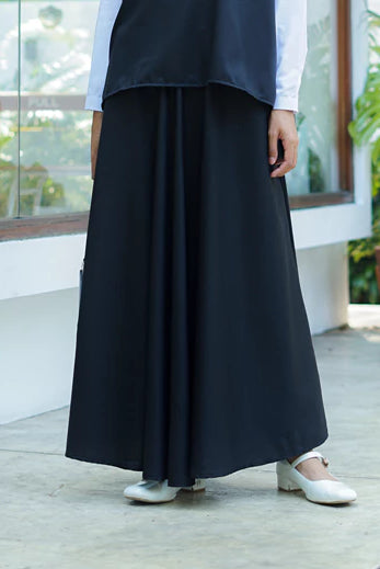 Person wearing a long black skirt by Abame with white shoes indoors.