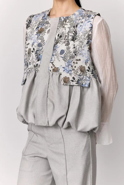 Person wearing a grey vest with floral details by Studio Tui on a plain background