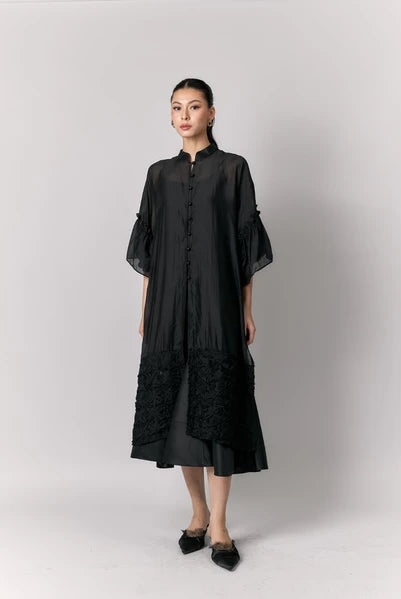 Woman wearing a black tunic by Studio Tui with sheer sleeves against a white background