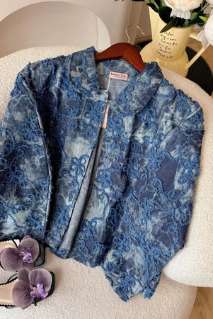 Dark jeans floral-patterned jacket from Haidee Orlin on a chair with a pair of shoes and a vase in the background.