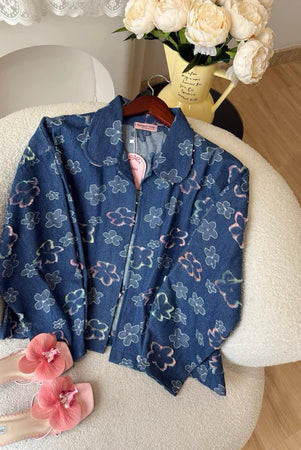 Blue floral-patterned denim jacket from Haidee Orlin on a chair with pink slippers and flowers in the background