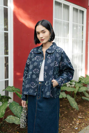 Woman wearing a Dark blue floral-patterned denim jacket from Haidee Orlin in front of a red wall with white trim.