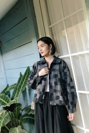 Woman wearing a black checkered denim jacket from Haidee Orlin standing in front of a building with plants around.