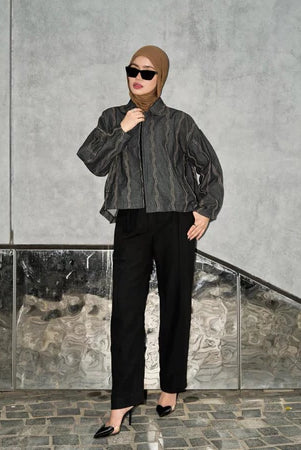 Woman wearing a black denim jacket with wave pattern from Haidee Orlin and sunglasses against a gray wall.