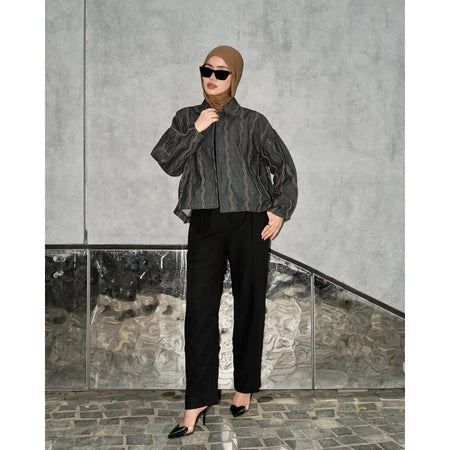 Woman wearing a black denim jacket with wave pattern from Haidee Orlin and sunglasses against a gray wall.