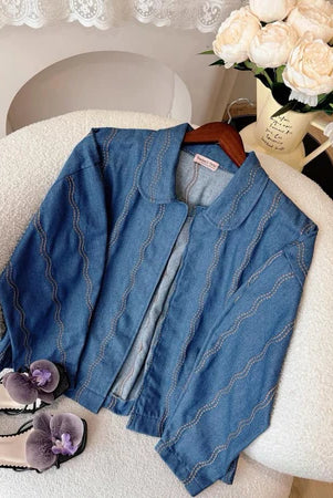 Blue denim jacket with a wavy pattern from Haidee Orlin on a chair with flowers and shoes in the background