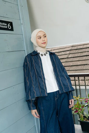 Woman wearing a dark blue denim jacket with wave pattern from Haidee Orlin and white hijab standing against a building with 'Richie House 6' sign.