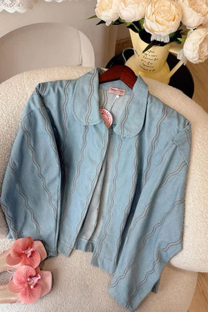 Light blue denim jacket with wave pattern from Haidee Orlin on a chair with a vase of flowers in the background