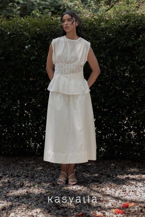 Woman wearing a white dress standing in front of greenery with 'kasyalia' branding.
