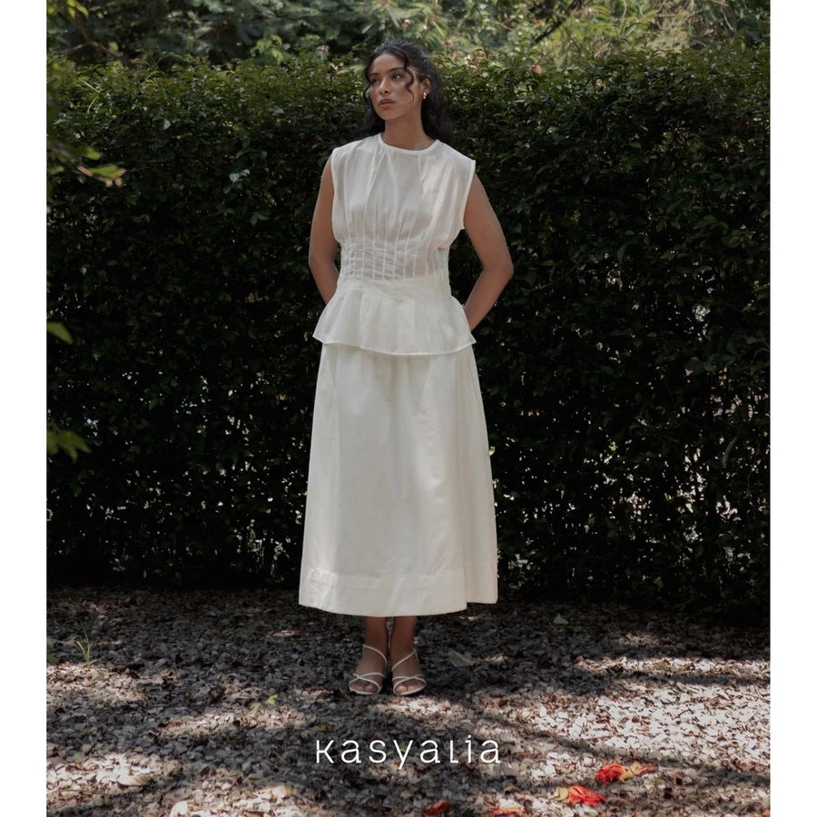 Woman wearing a white dress standing in front of greenery with 'kasyalia' branding.