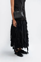 Person wearing a black ruffled skirt and black shoes with a black grain leather handbag by Aesthetic Pleasure on a white background