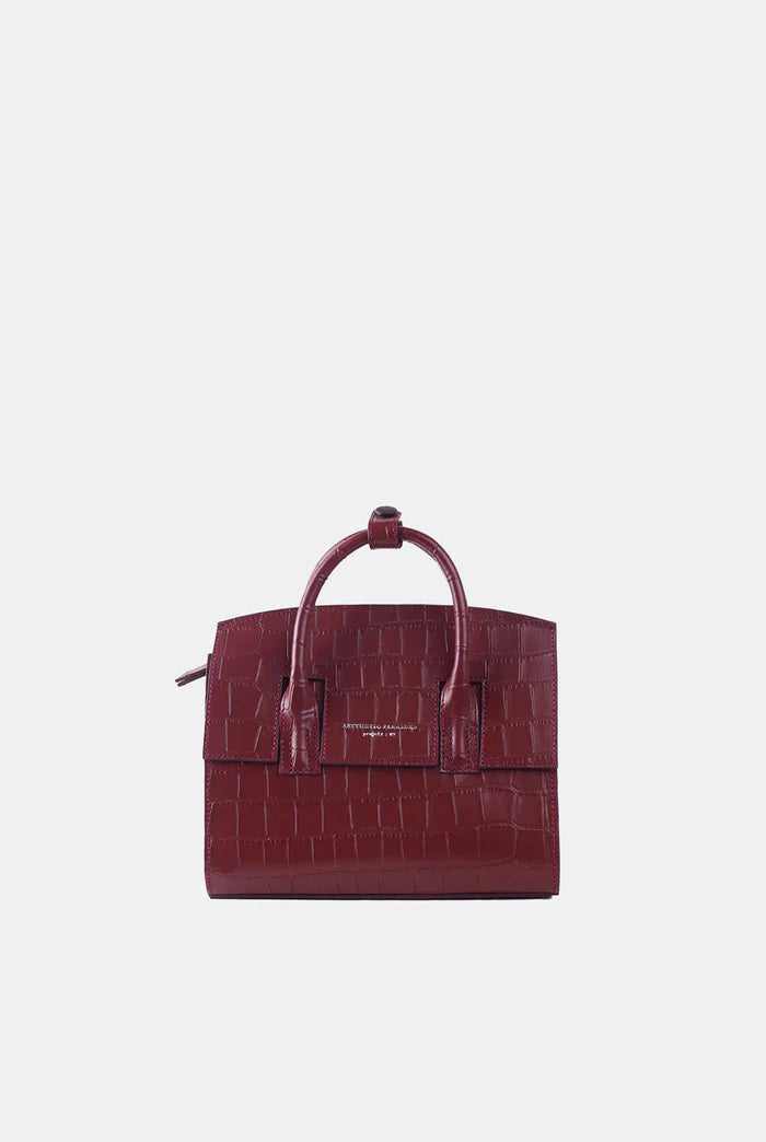 A mini-sized maroon leather handbag with a textured alligator pattern, featuring a detachable strap and silver-tone hardware by Aesthetic Pleasure.