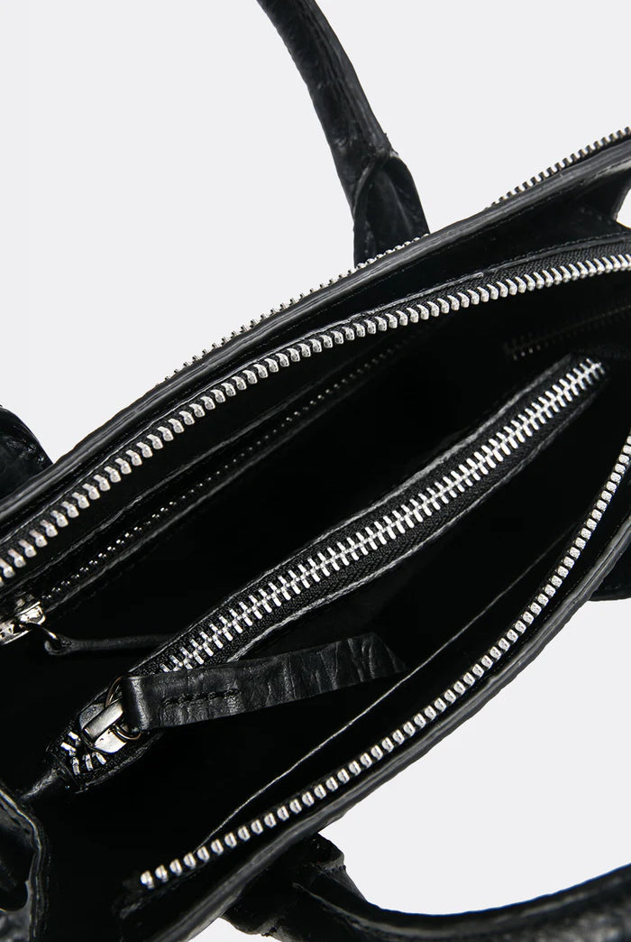 Close-up of a black leather mini handbag by Aesthetic Pleasure with zippers on a white background