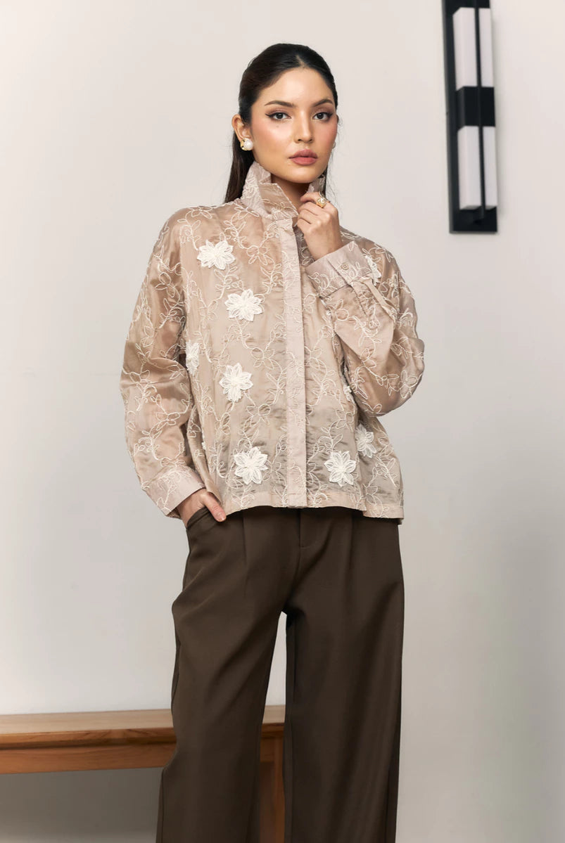 Woman wearing a brown floral shirt by Studio Tui and brown pants against a plain background