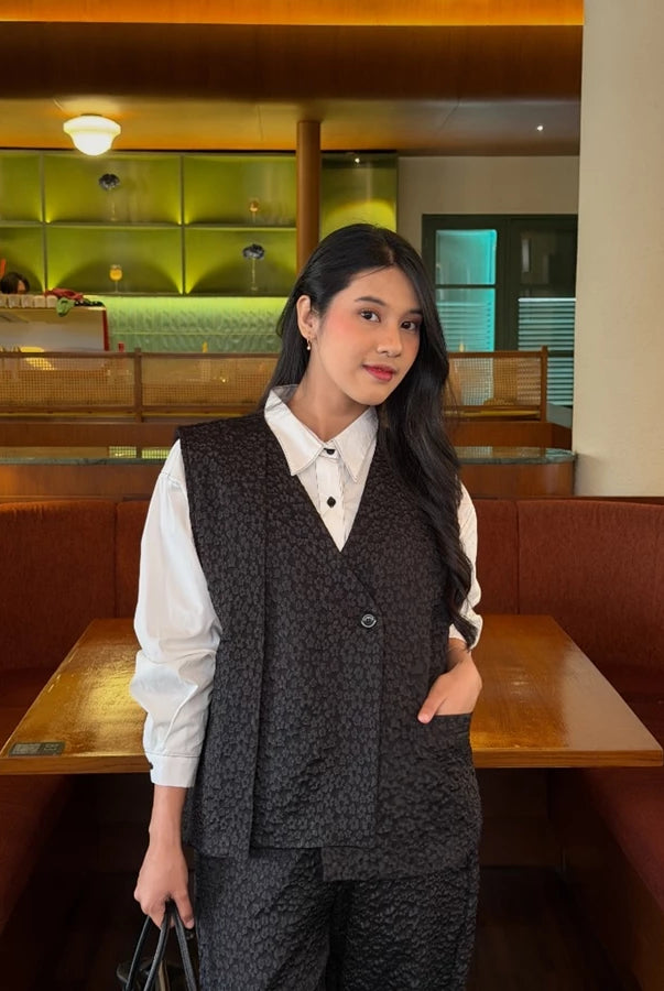 Woman in a patterned black vest over a white shirt standing in a restaurant setting