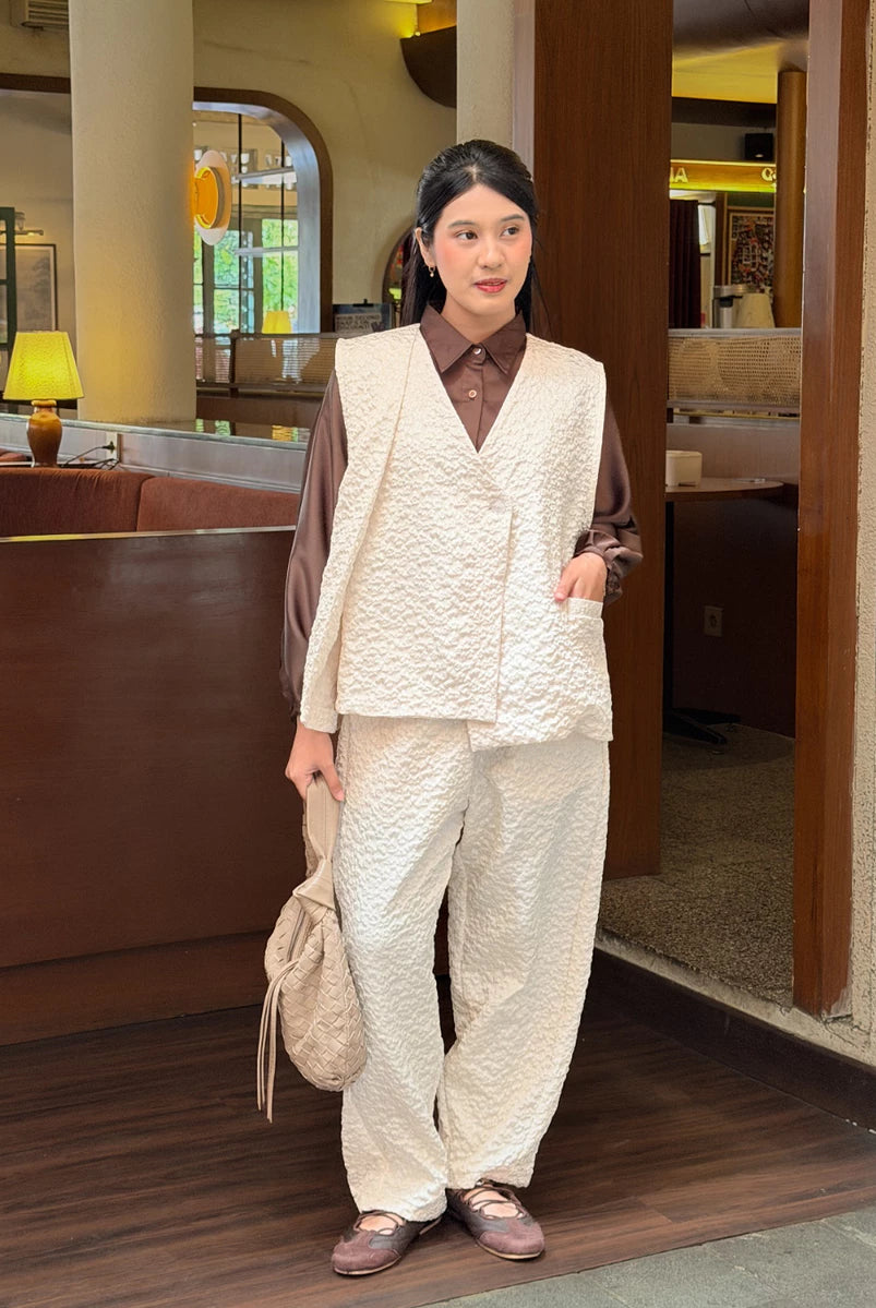 Person wearing a brown shirt with a broken white vest and pants in an indoor setting.