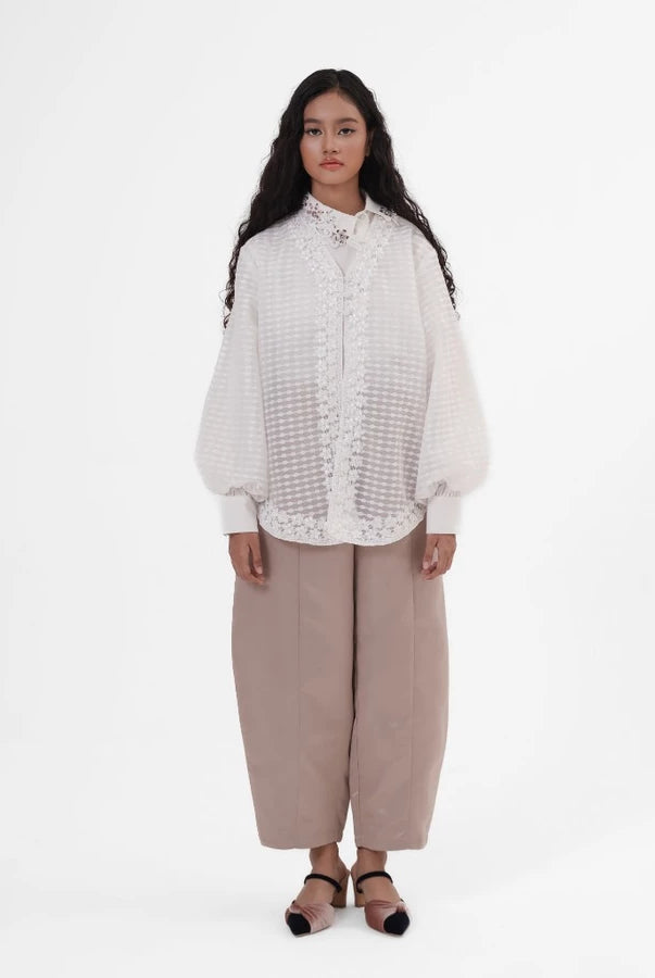 Woman wearing a white outer by Jenna & Kaia and beige pants on a white background