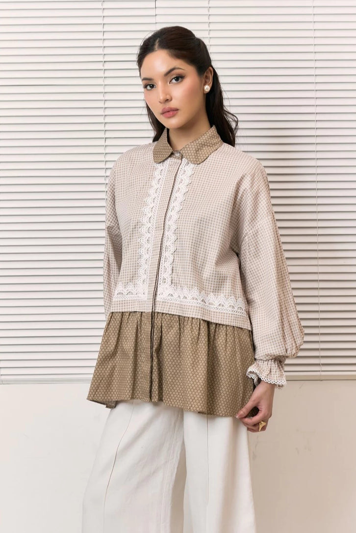 A woman models a beige and brown patterned shirt by Studio Tui with white lace trim and white wide-leg pants, standing in front of white window blinds.
