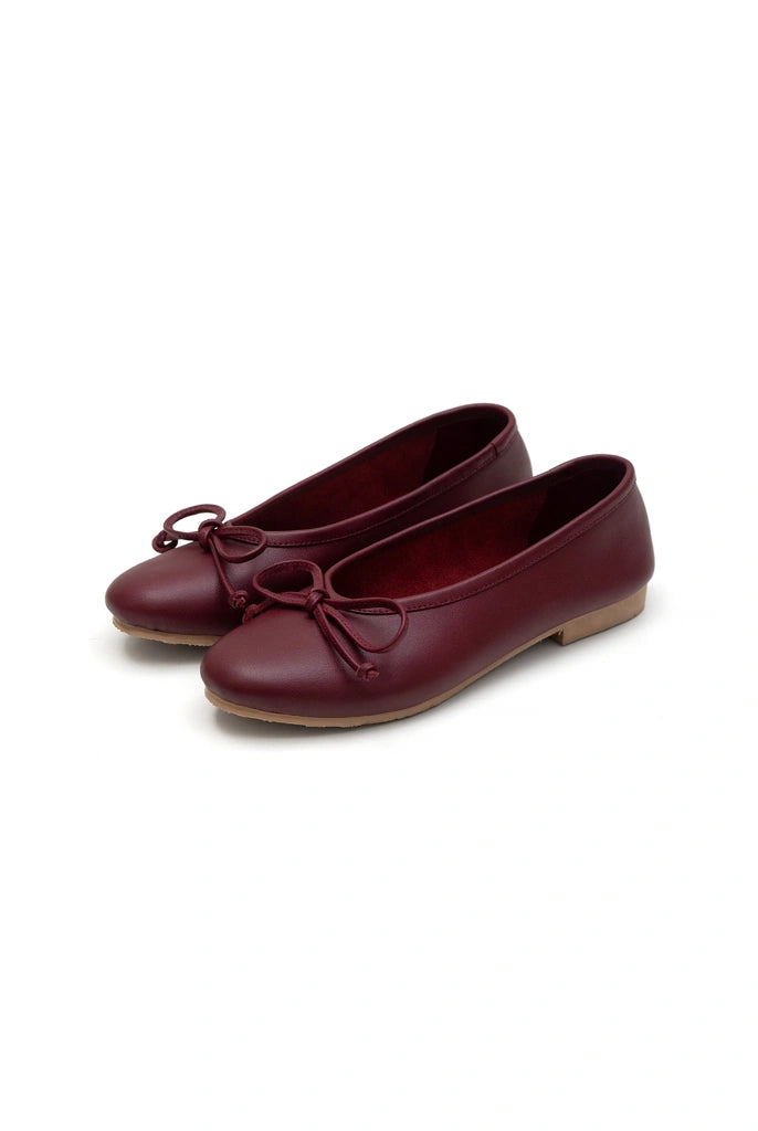 Pair of maroon flat shoes by Cajsa with a bow on a white background