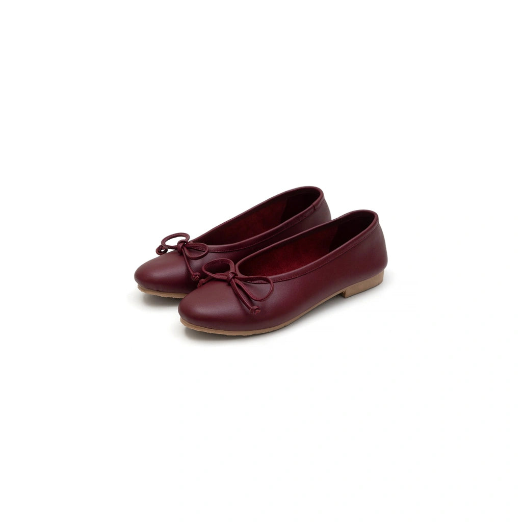 Pair of maroon flat shoes by Cajsa with a bow on a white background