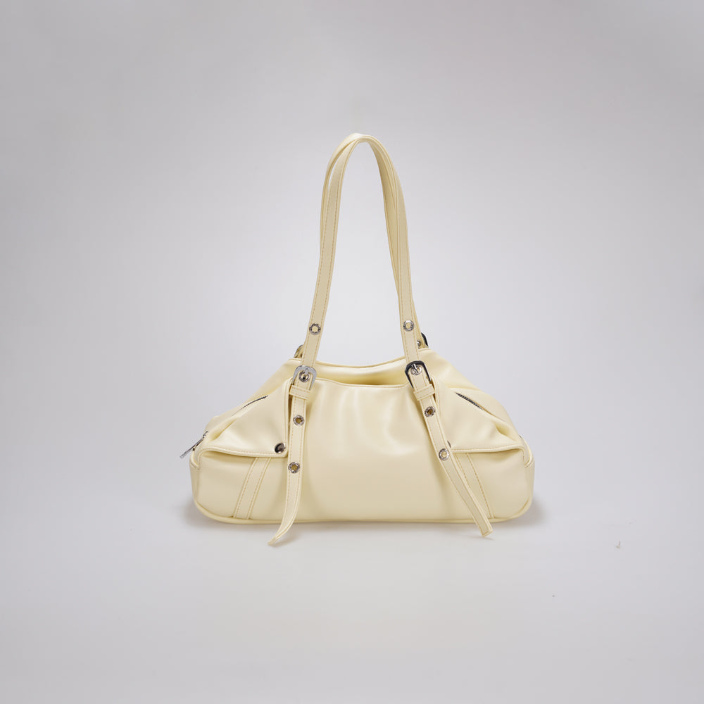 A cream-colored leather shoulder bag by Cekhas with a curved top handle, decorative buckle straps, and silver-tone hardware, shown against a neutral light gray background.