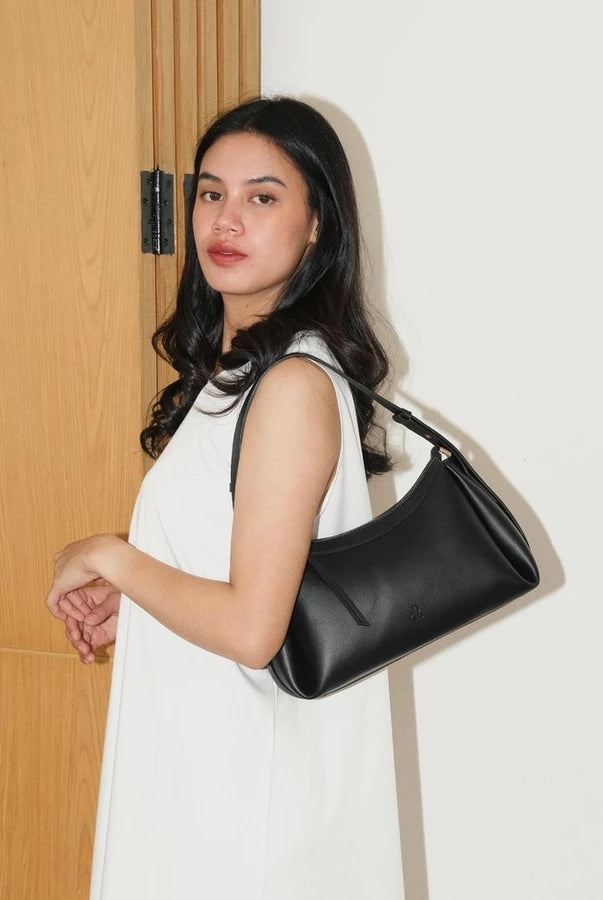 Woman holding a black handbag by Prior against a white wall.