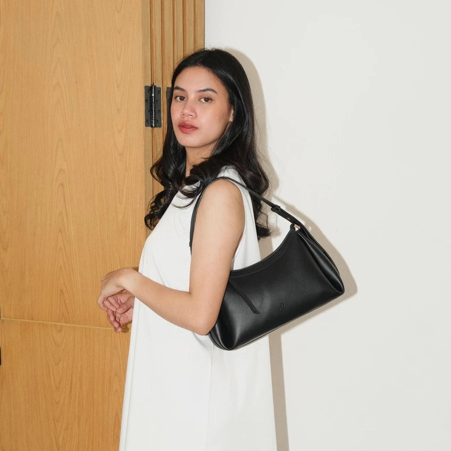 Woman holding a black handbag by Prior against a white wall.