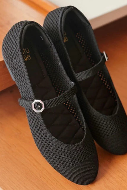 Pair of black mesh flatshoes with a strap by Tutu Toe on a wooden floor