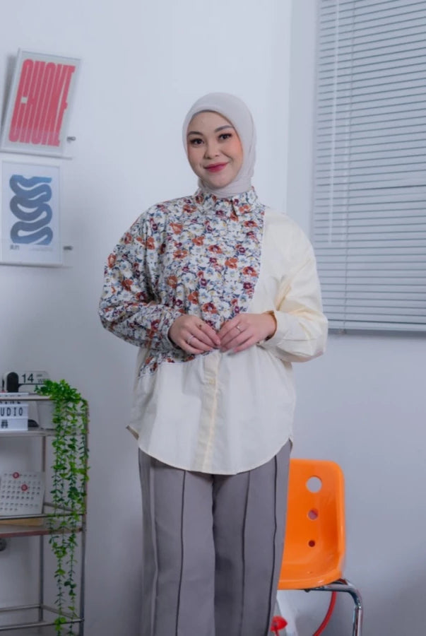 Woman wearing a floral shirt by Abame over a white shirt with gray pants in an office setting.