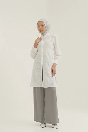 Seorang wanita menggunakan Mosa Tuniq, sebuah premium tunik dengan material cotton embroidery dan terdapat pita belakang yang bisa disesuaikan dengan badan, dari brand Tunique