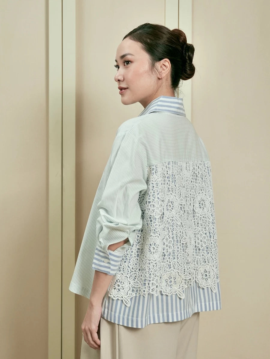 Woman wearing a light blue-colored striped shirt by Studio Tui with lace details on the back against a beige background