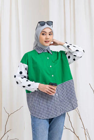 Woman wearing a green, polka dot, and checkered shirt by Abame against a white curtain background