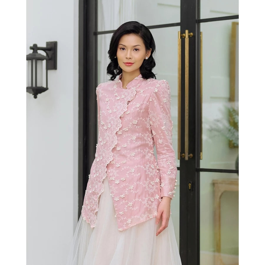 Woman wearing a pink embroidered blouse by Kasa Heritage and white skirt standing in front of a glass door.