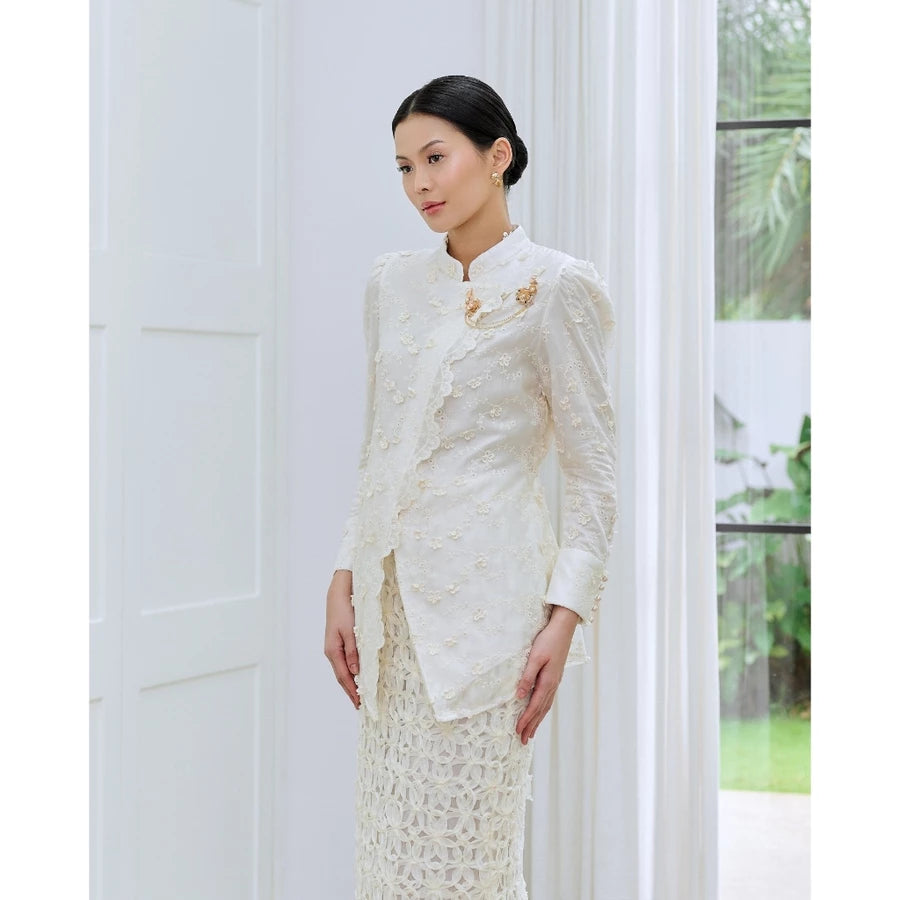 Woman wearing a ivory white lace blouse by Kasa Heritage standing in a room with white walls and a window.