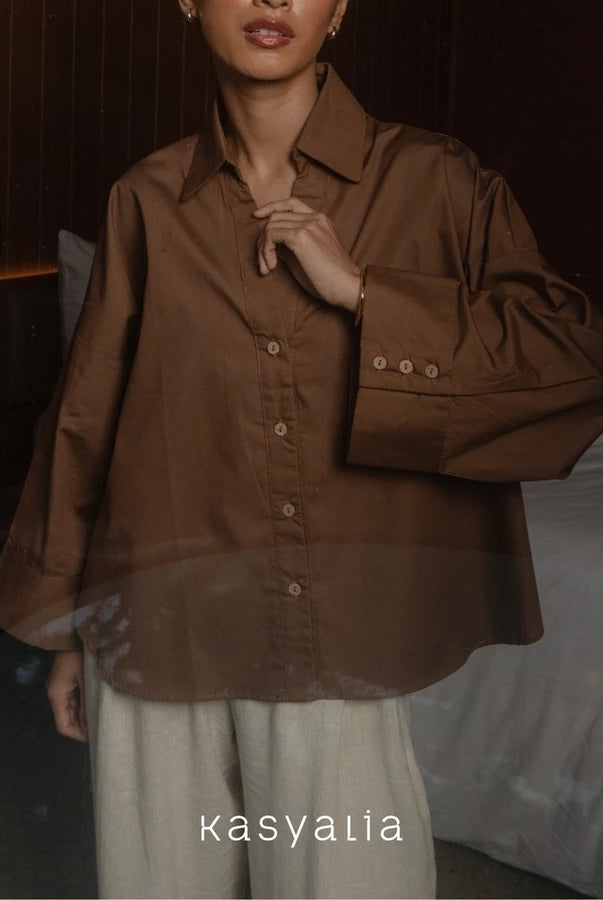 Person wearing a brown button-up shirt with a blurred background, featuring the brand 'kasyalia'.
