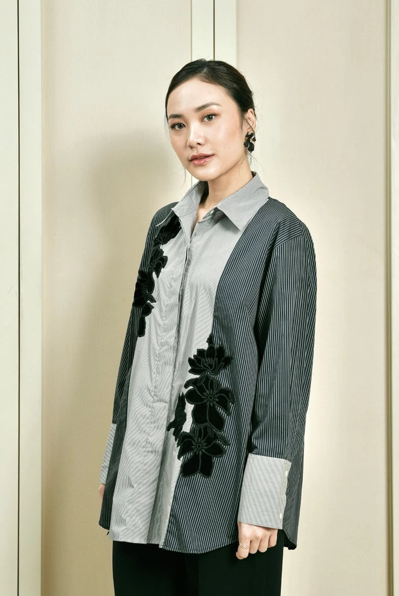 Woman wearing a stylish blue and grey shirt by Studio Tui with floral details against a neutral background
