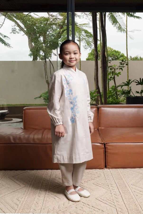 Child in a white tunic by Jenna & Kaia standing in front of a brown leather sofa with a garden view.
Seorang anak mengenakan tunik putih karya Jenna & Kaia berdiri di depan sofa kulit cokelat dengan pemandangan taman.