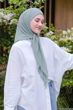 Woman wearing a light green pashmina hijab by Puru Kambera and white shirt outdoors with greenery in the background
