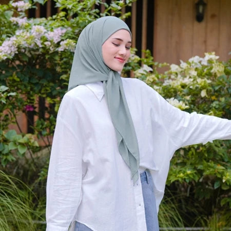 Woman wearing a light green pashmina hijab by Puru Kambera and white shirt outdoors with greenery in the background