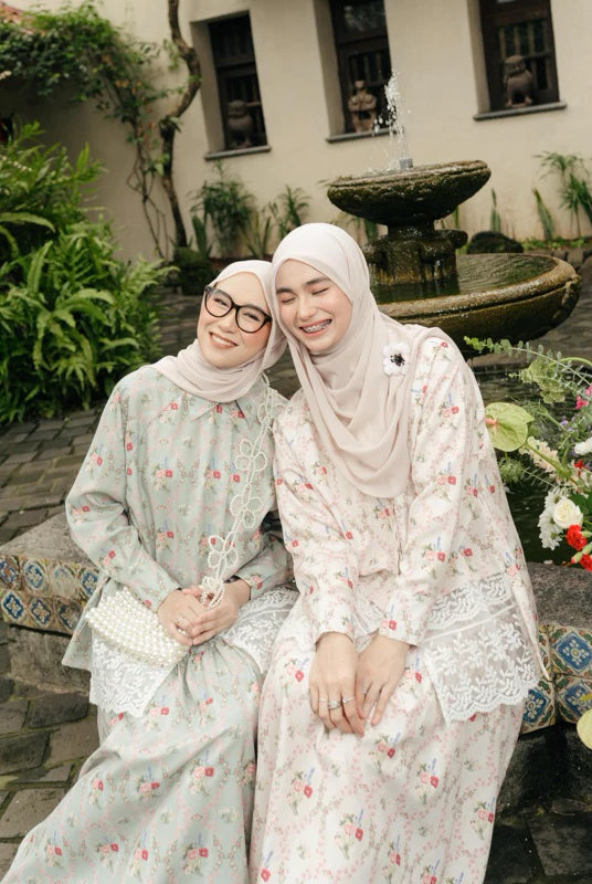 Two women in floral dresses and Narnia Skirt from Haidee Orlin sitting together in a garden with a fountain in the background.