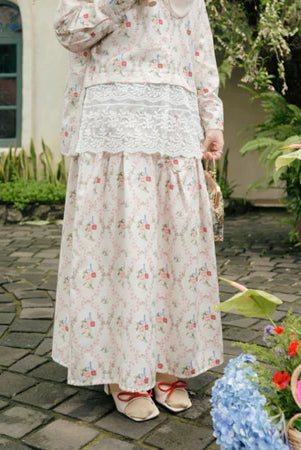 Person wearing a cream floral dress and skirt from Haidee Orlin standing outdoors on a stone path with plants and flowers.
