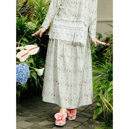 Person wearing a light green floral dress and skirt from Haidee Orlin standing in a garden with flowers and plants.