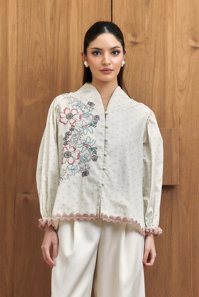Woman wearing a white embroidered blouse with floral patterns by Studio Tui against a wooden background