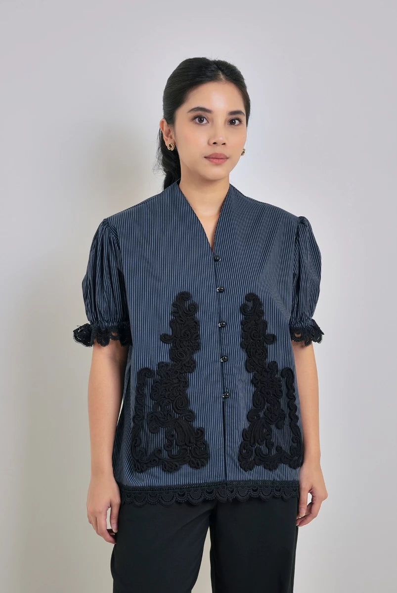Woman wearing a striped blue blouse with black lace details by Studio Tui on a plain background