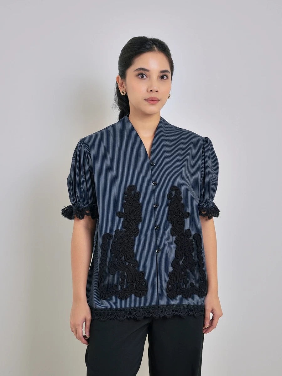 Woman wearing a striped blue blouse with black lace details by Studio Tui on a plain background