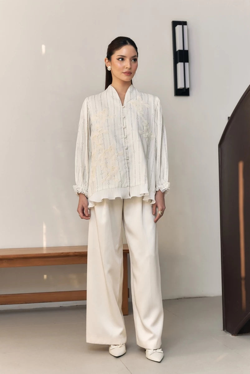 Woman wearing a white embroidered blouse by Studio Tui in a minimal indoor setting