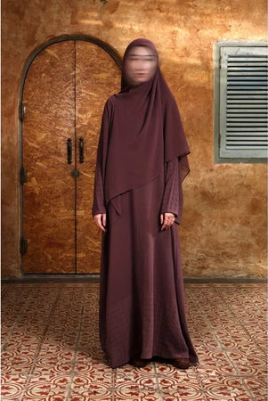Person wearing a burgundy Mecca Dhurma Abaya by Nehhat Modest in front of a wooden door.