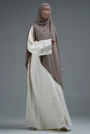 Person wearing a light brown hijab by Nehhat Modest and white abaya on a gray background