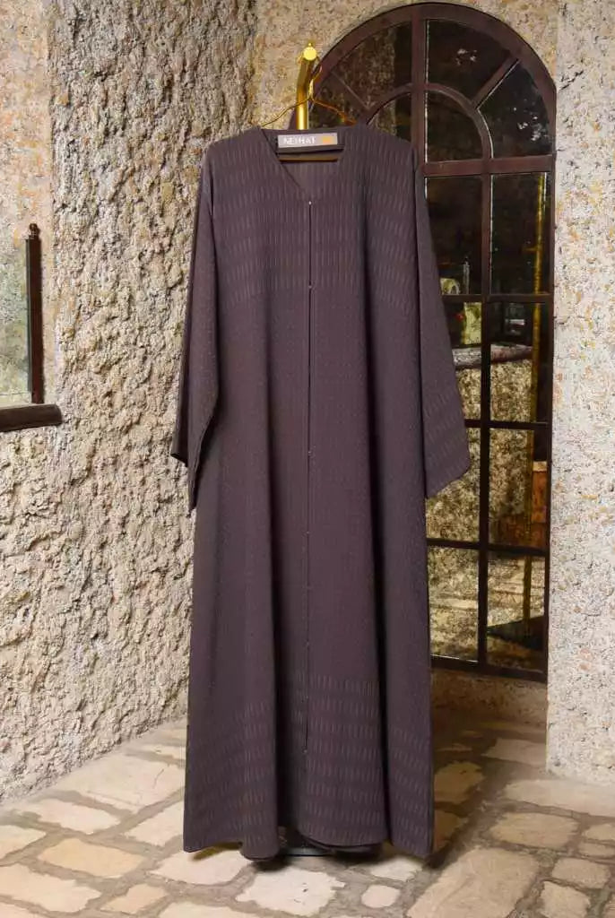 Long dark purple abaya by Nehhat Modest hanging on a stone wall with a mirror.